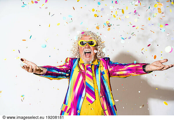 Cheerful man enjoying with confetti against white background