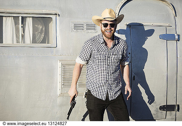 Cheerful man holding gun while standing against camper van