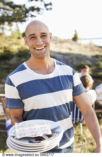 Cheerful man holding plates with friends in background