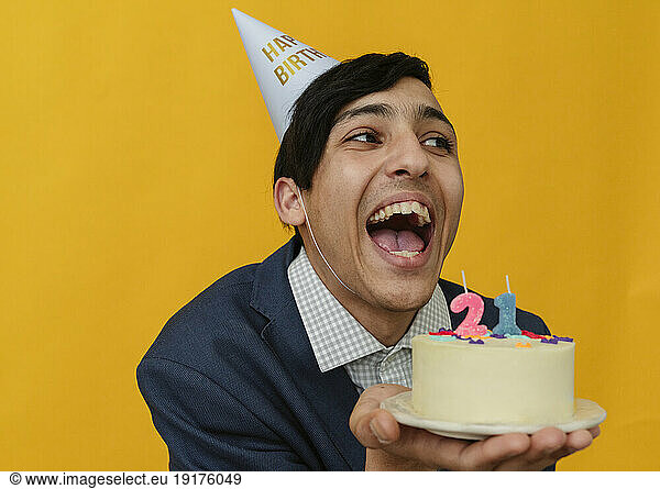 Cheerful man holding 21st birthday cake in studio