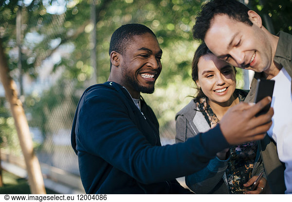 Cheerful man showing mobile phone to friends
