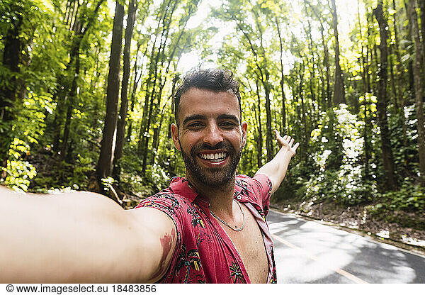 Cheerful man taking selfie on road in front of trees