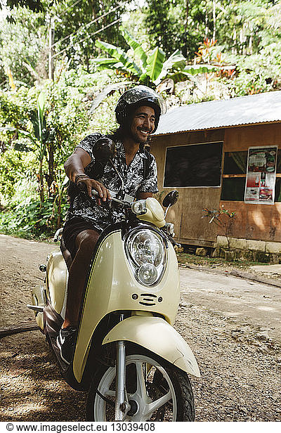 Cheerful man wearing helmet while driving motor scooter on dirt road