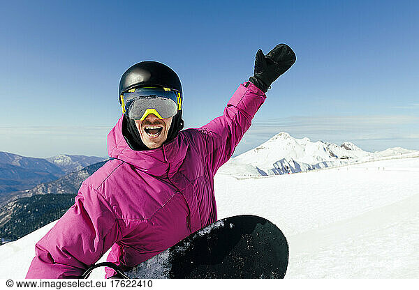 Cheerful man with hand raised enjoying at ski resort