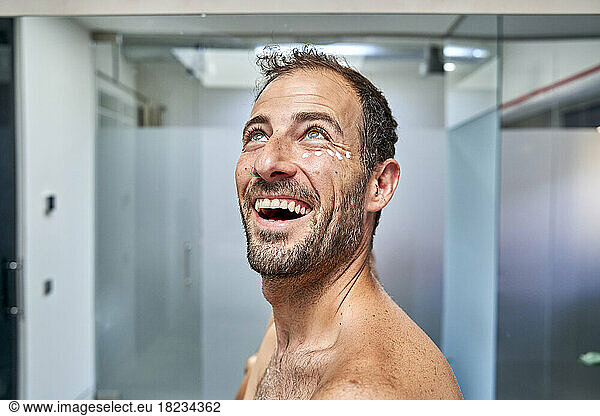 Cheerful man with moisturizer cream on face in bathroom at home