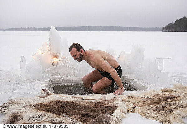 Cheerful mature man enjoying ice bath at frozen lake during vacation