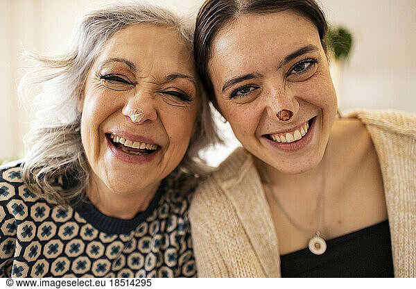 Cheerful mature woman and daughter with food smears on nose having fun at home