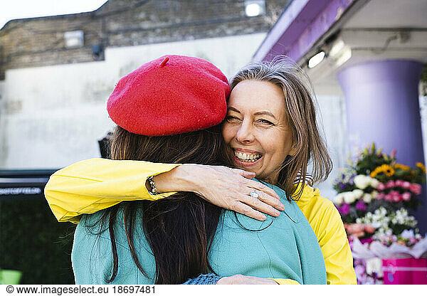 Cheerful mature woman embracing female friend by flower shop