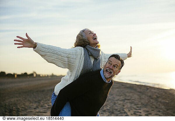Cheerful mature woman enjoying piggyback ride at beach