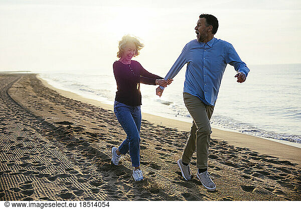 Cheerful mature woman running with man at coastline