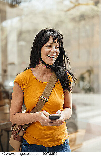 Cheerful mature woman standing with smart phone