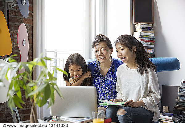 Cheerful mother and daughters doing video call with laptop at home