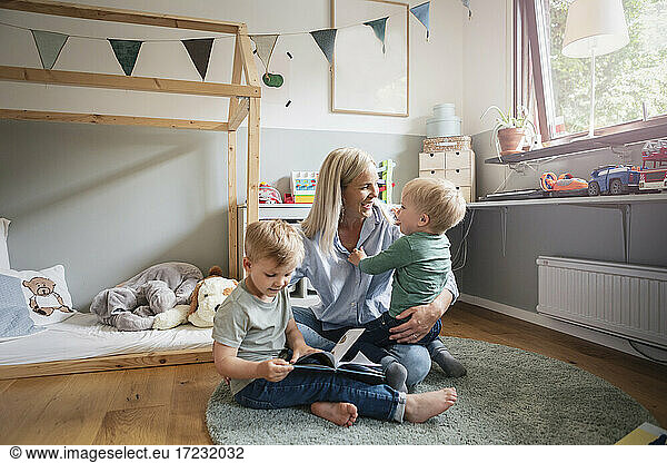 Cheerful mother playing with children in bedroom