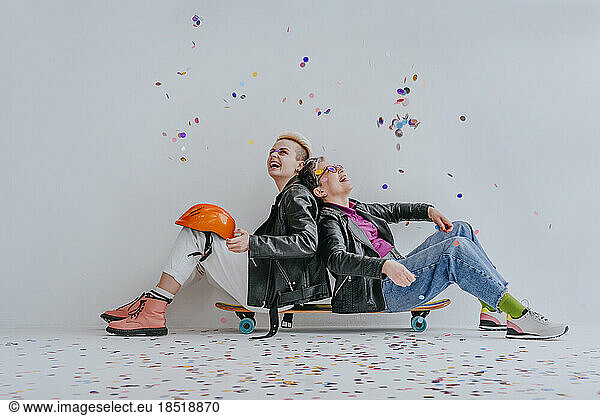 Cheerful mother throwing confetti with daughter sitting on longboard