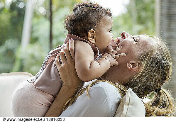 Cheerful mother with baby daughter embracing each other at home