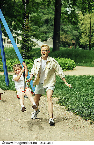 Cheerful mother with daughter swinging on swing at playground