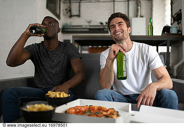 Cheerful multicultural friends drinking beer and watching football match