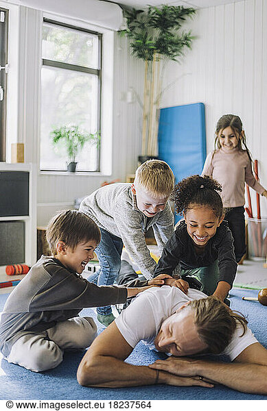 Cheerful multiracial children playing with male teacher in day care center