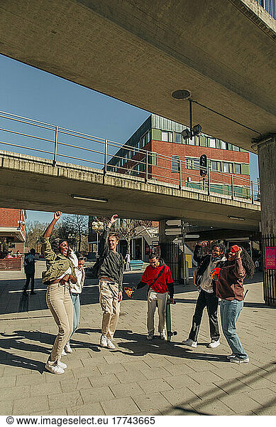 Cheerful multiracial friends enjoying dance below bridge at street on sunny day