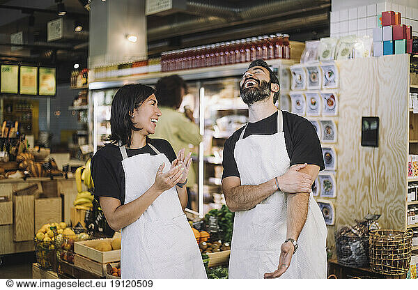 Cheerful multiracial male and female retail clerks wearing aprons standing at grocery store