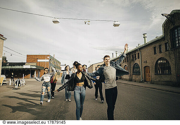 Cheerful multiracial young friends dancing while walking on street in city