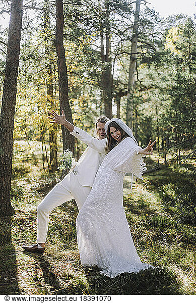 Cheerful newlywed bride and groom gesturing in forest