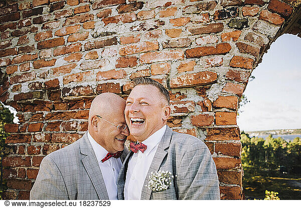 Cheerful newlywed gay couple enjoying against brick wall