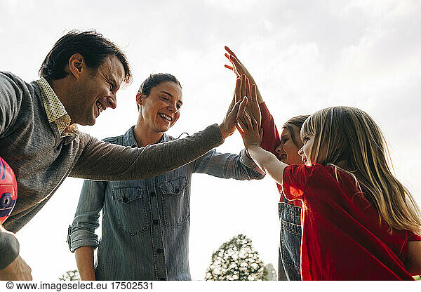 Cheerful parents doing high-five with daughters in park