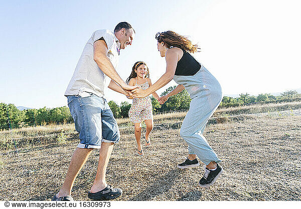Cheerful parents playing with daughter on land against clear sky