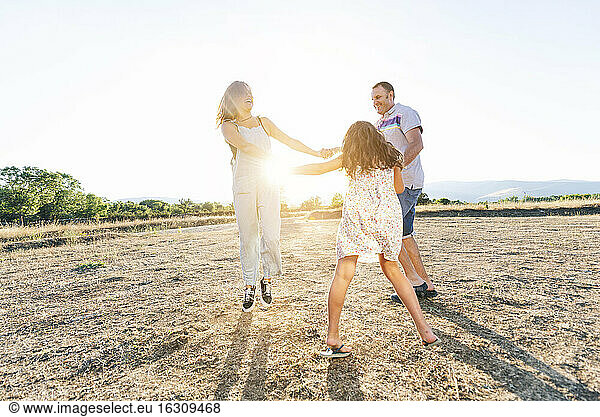 Cheerful parents playing with daughter on land against clear sky during sunny day