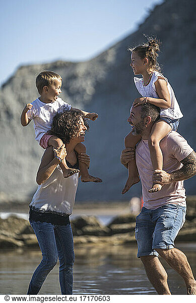 Cheerful parents with kids on shoulder enjoying at beach