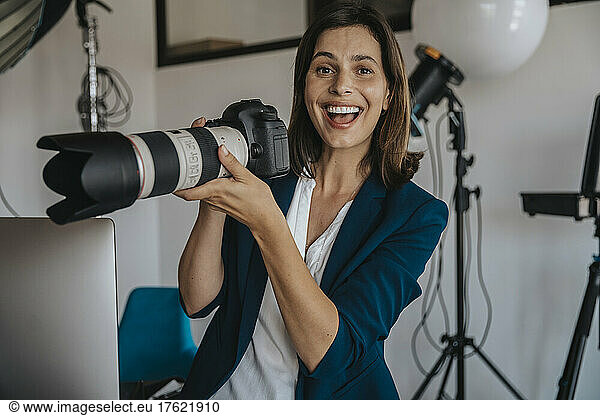 Cheerful photographer holding digital camera in studio