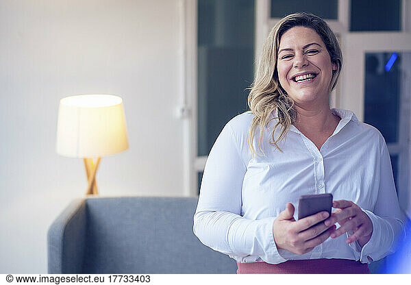 Cheerful plus size businesswoman with mobile phone at work place