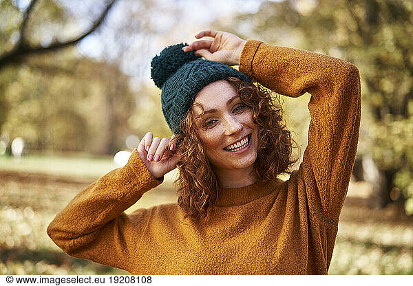 Cheerful redhead woman wearing knit hat at autumn park