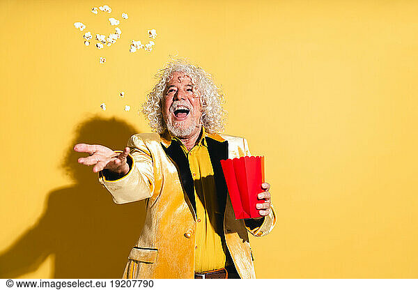 Cheerful senior man catching popcorn against yellow background