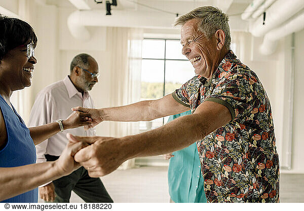Cheerful senior man holding hands of woman while dancing in class