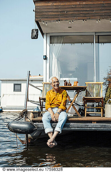 Cheerful senior man sitting at houseboat enjoying on sunny day