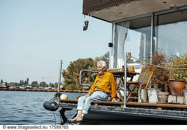 Cheerful senior man sitting at houseboat on sunny day