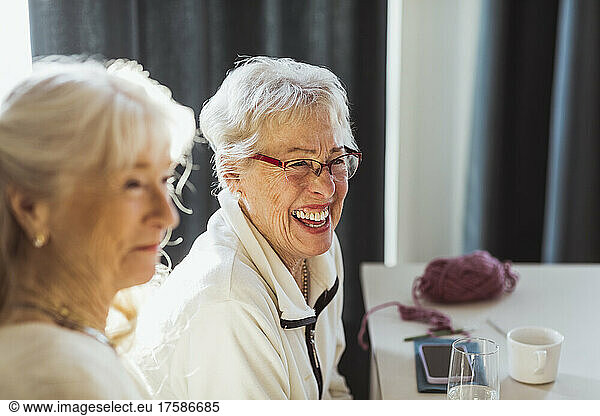 Cheerful senior woman sitting by female friend in nursing home
