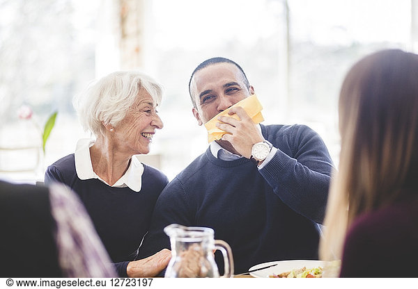 Cheerful senior woman with son wiping mouth with tissue paper while having lunch in nursing home