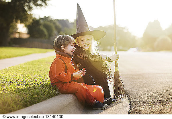 Cheerful siblings dressed for halloween party sitting by road