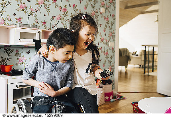 Cheerful sister watching video with autistic brother on smart phone at home