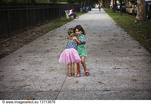 Cheerful sisters embracing on footpath at park