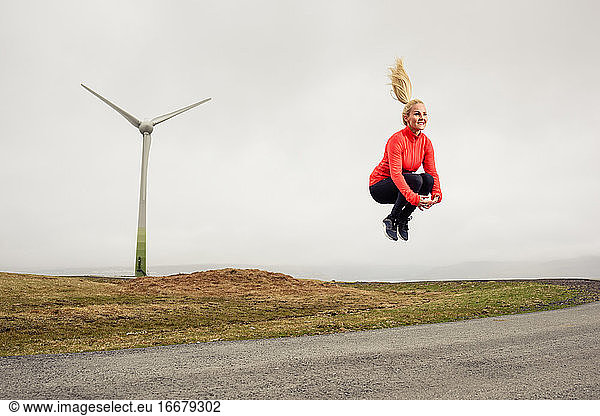 Cheerful sportswoman jumping over road in countryside