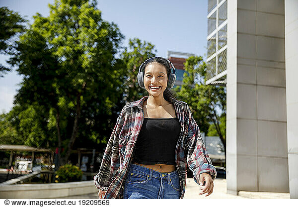 Cheerful student walking and listening to music through wireless headphones