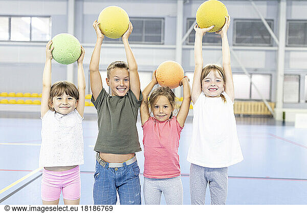 Cheerful students with arms raised holding ball standing together at school sports court