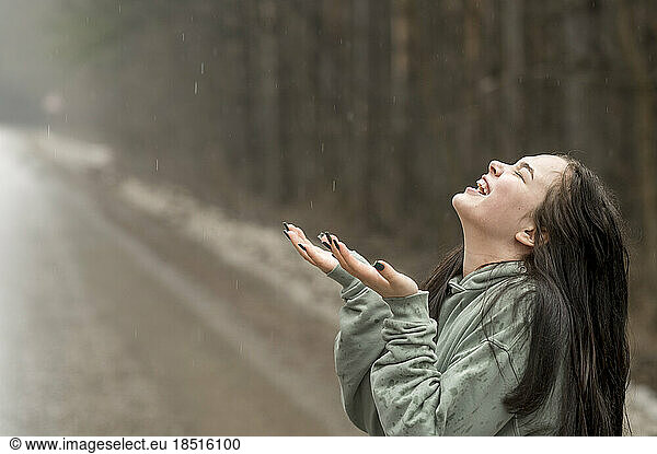 Cheerful teenage girl enjoying rain on road