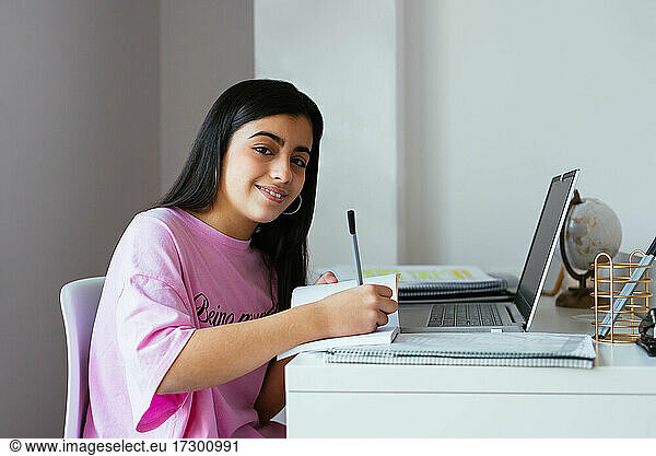 Cheerful teenager studying at desk in own room