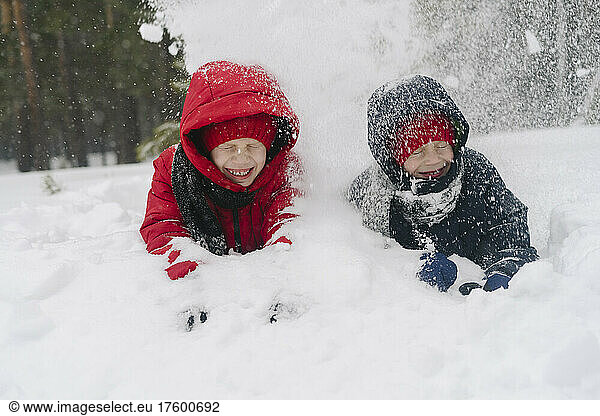 Cheerful twin brothers throwing snow on each other in forest