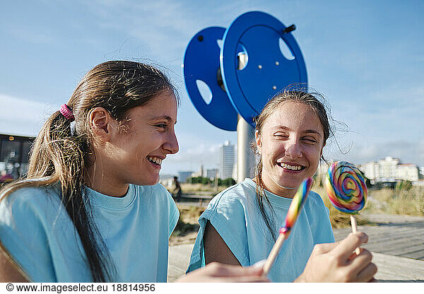 Cheerful twin sisters enjoying lollipop candy at beach